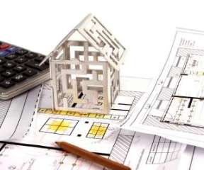 Desktop with scattered house plans, a calculator and a small stylized house model